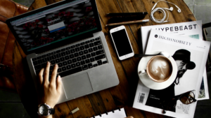 View from above of someone using a laptop at a desk filled with coffee, magazines, and their phone.