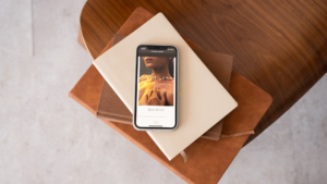 A phone featuring a photo of a woman on a website, stacked atop books in coordinating colors.