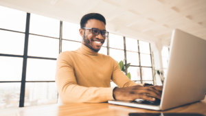 A smiling man using a computer while sitting at a desk