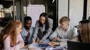Employees sit together discussing around a desk with papers.